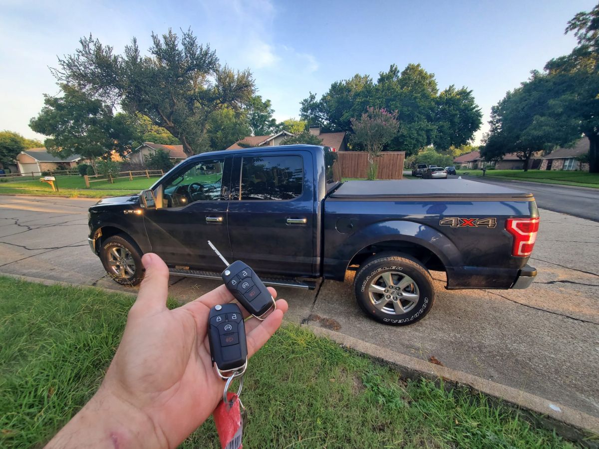 Mobile locksmith holding two Ford flip keys in front of a customer's F-150 truck